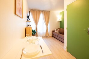 Un coin repas avec une table dressée pour quatre personnes, un canapé, une porte verte et une plante.