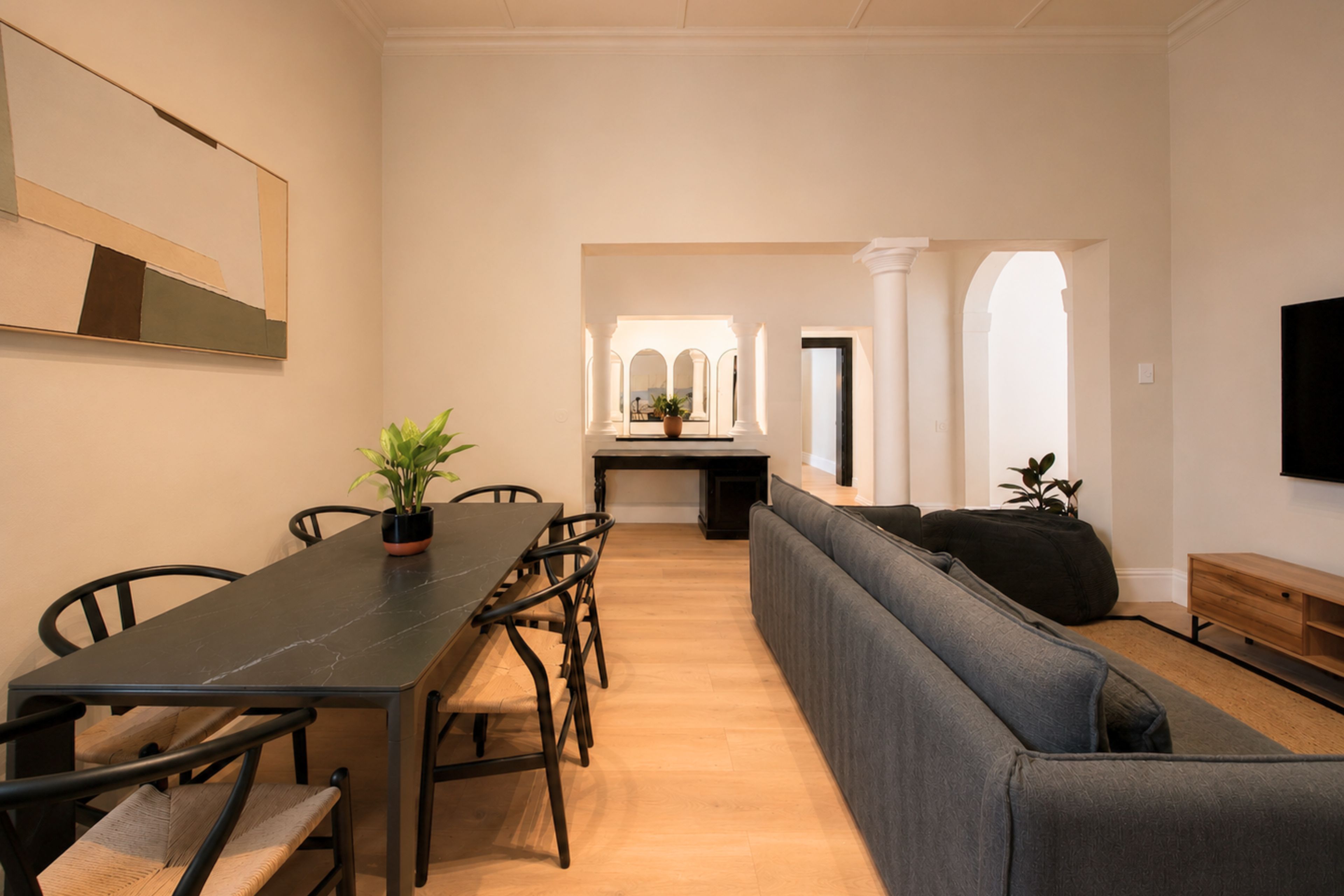 A modern living room with a dining area, a sofa, a TV, and a plant.