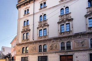 Un immeuble à plusieurs étages, doté d’éléments architecturaux classiques, notamment des sculptures décoratives et des fenêtres en arc de cercle.