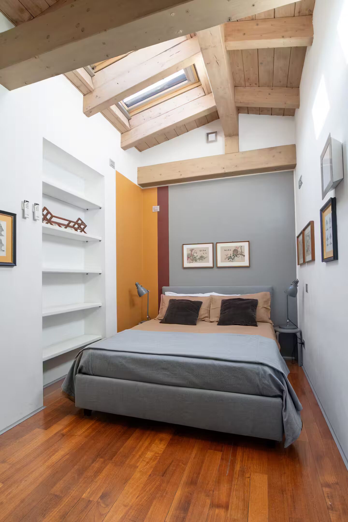 Un dormitorio con tragaluz, una cama, una mesita de noche y estantes en la pared.