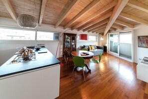 A modern kitchen with a central island, wooden beams on the ceiling, and a dining area with a round table and chairs. - Brera Penthouse - View of Porta Nuova (Milano)