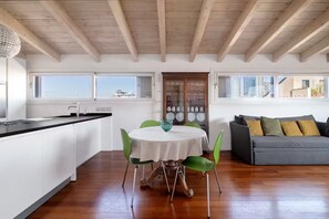 A modern kitchen with a dining area, wooden ceiling beams, and a view of the city. - Brera Penthouse - View of Porta Nuova (Milano)