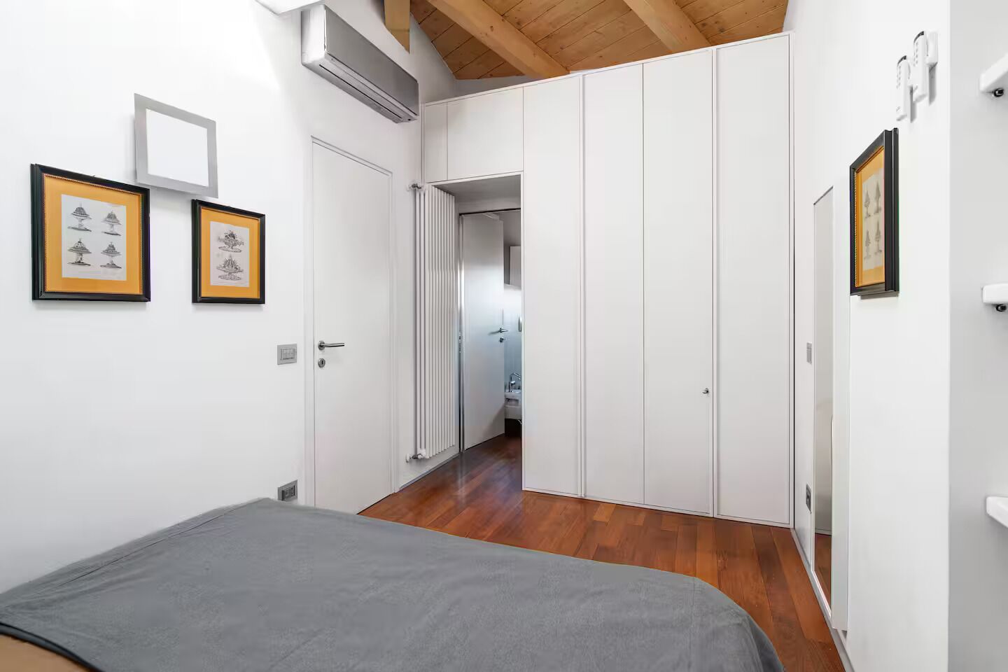 A bedroom with a bed, white wardrobe, and framed pictures on the wall.