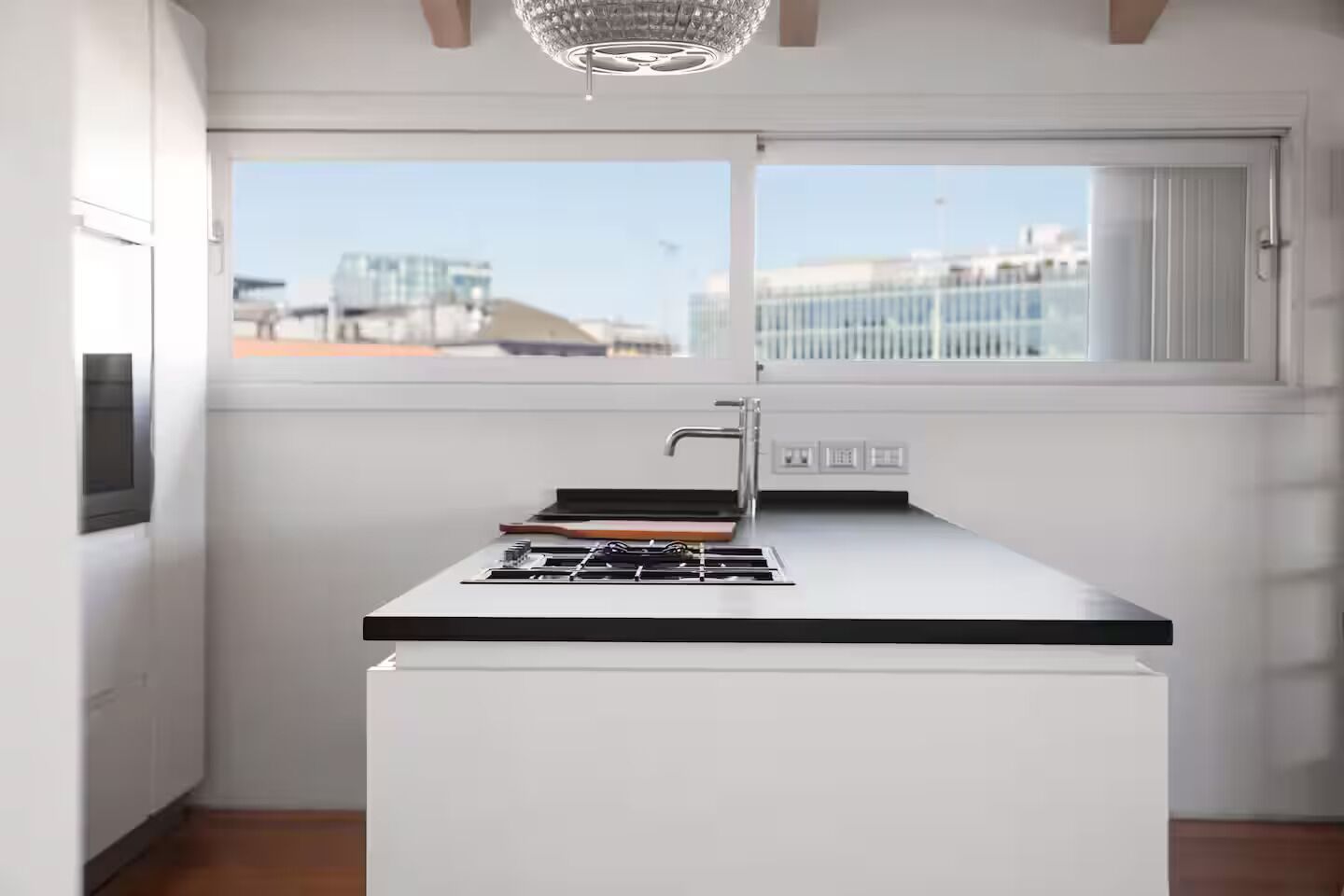 Una cocina moderna con estufa a gas, un lavamanos y un ventanal con vistas a edificios.