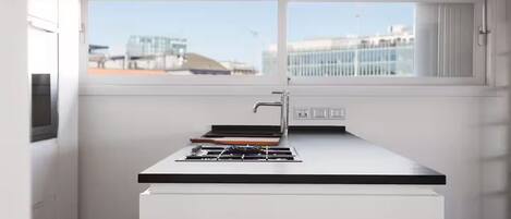 Una cocina moderna con estufa a gas, un lavamanos y un ventanal con vistas a edificios.