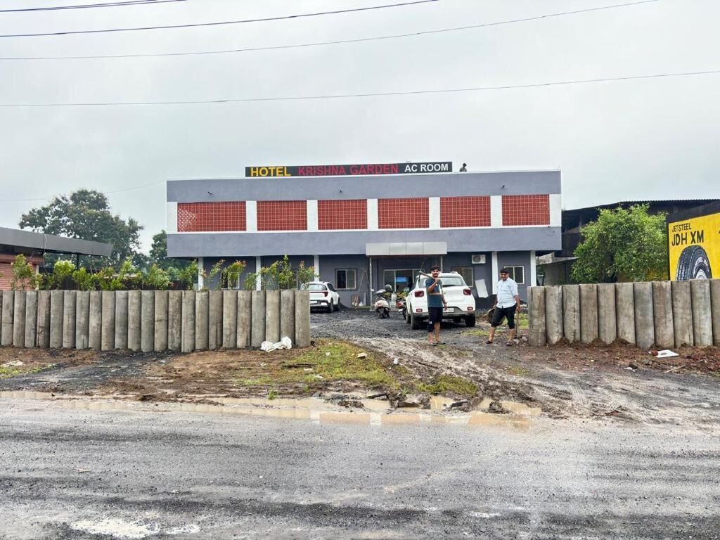 A hotel named 'Krishna Garden' with an AC room, a concrete fence, and a dirt road in front.