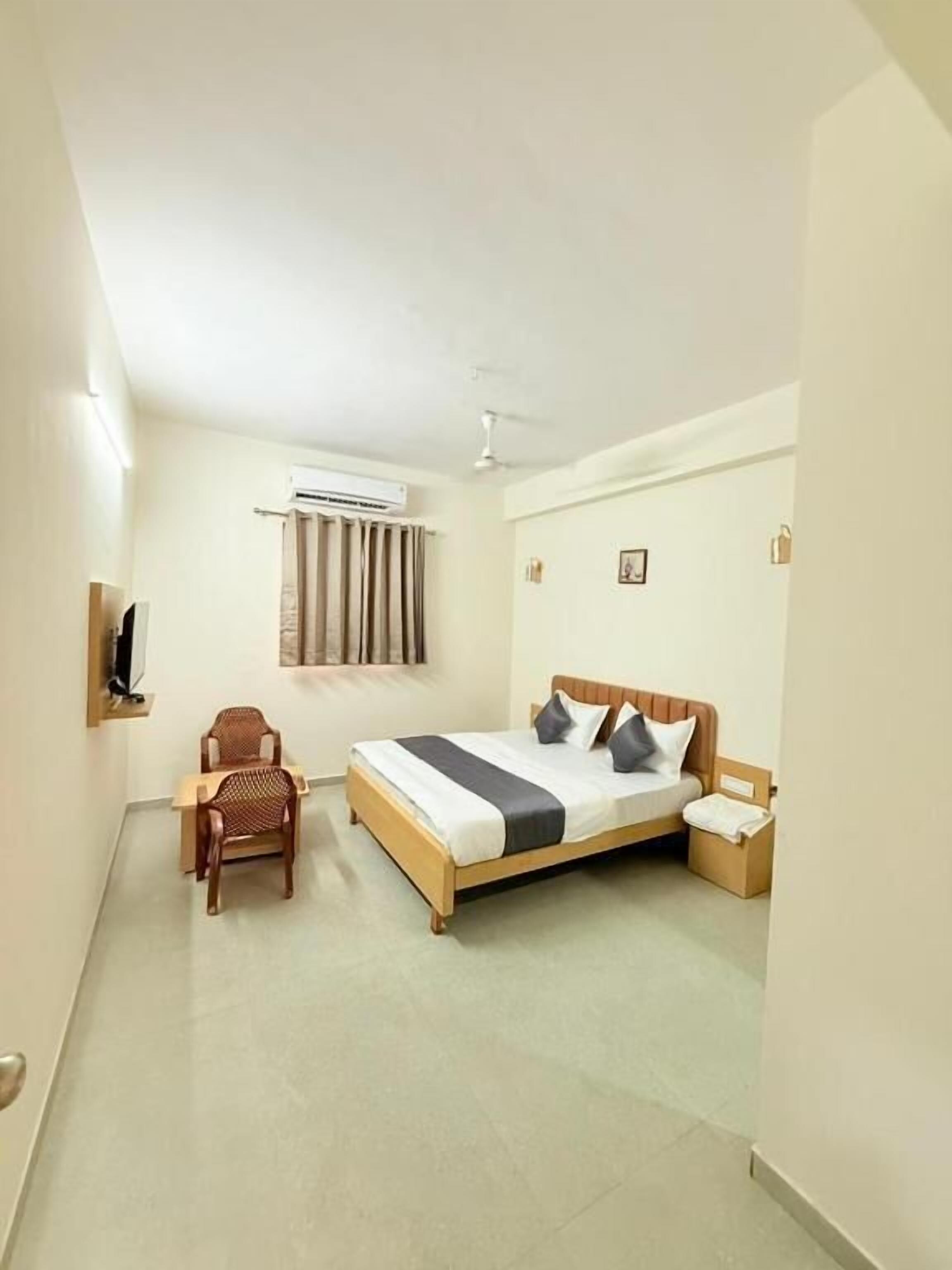 Habitación de hotel con cama, una silla, mesita de noche, equipo de aire acondicionado y ventana con cortinas.