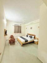 Habitación de hotel con cama, una silla, mesita de noche, equipo de aire acondicionado y ventana con cortinas.