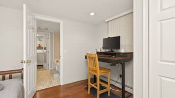 A room with a bed, a desk with a computer and a chair, a door leading to another room, and a small rug on the floor.