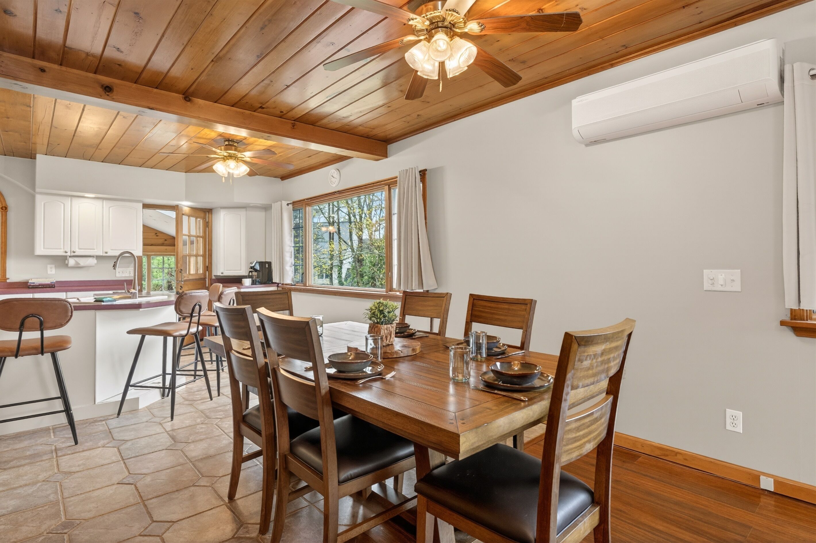 A wooden dining table with chairs, a ceiling fan, and a window with curtains.