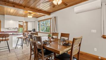 A wooden dining table with chairs, a ceiling fan, and a window with curtains.