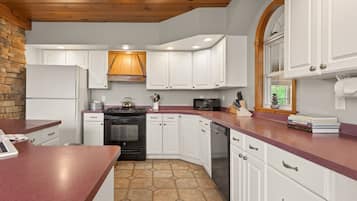 A kitchen with white cabinets, a stone backsplash, a wooden ceiling, and a red countertop.