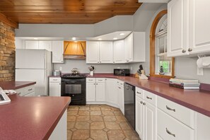 A kitchen with white cabinets, a stone backsplash, a wooden ceiling, and a red countertop. - Canandaigua Lake | Near Wineries | Sleeps up to 10 | Hot tub (Rushville)