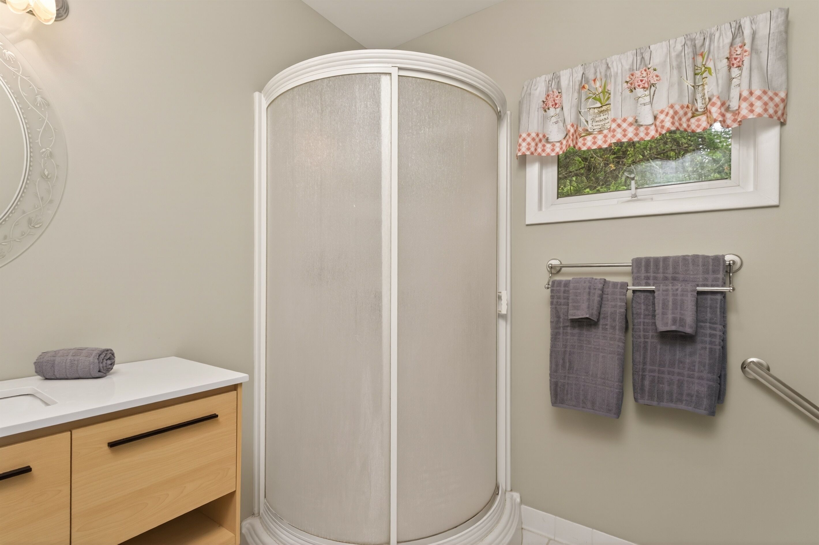 Een badkamer met douchecabine, een wastafel met handdoek en een raam met bloemen gordijn.