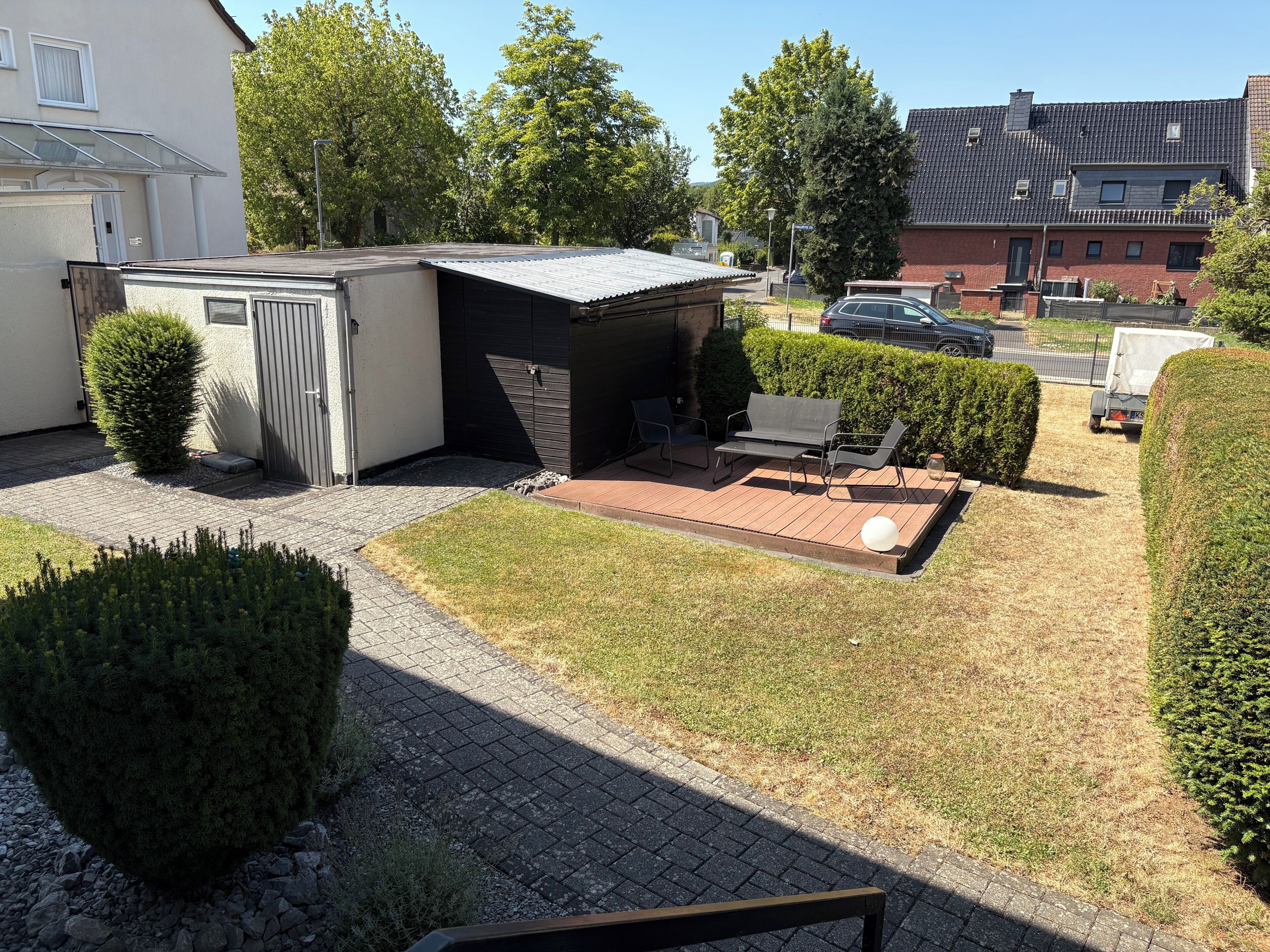 Ein Wohngebiet mit einer kleinen Terrasse, einem Geräteschuppen und einem geparkten Auto in der Nähe.