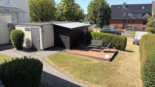 Et boligområde med en lille terrasse, et skur og en bil parkeret i nærheden.