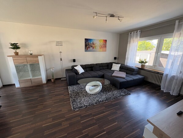 Una sala de estar moderna con un sofá modular, un aparador de vidrio, un cuadro y vistas al exterior.