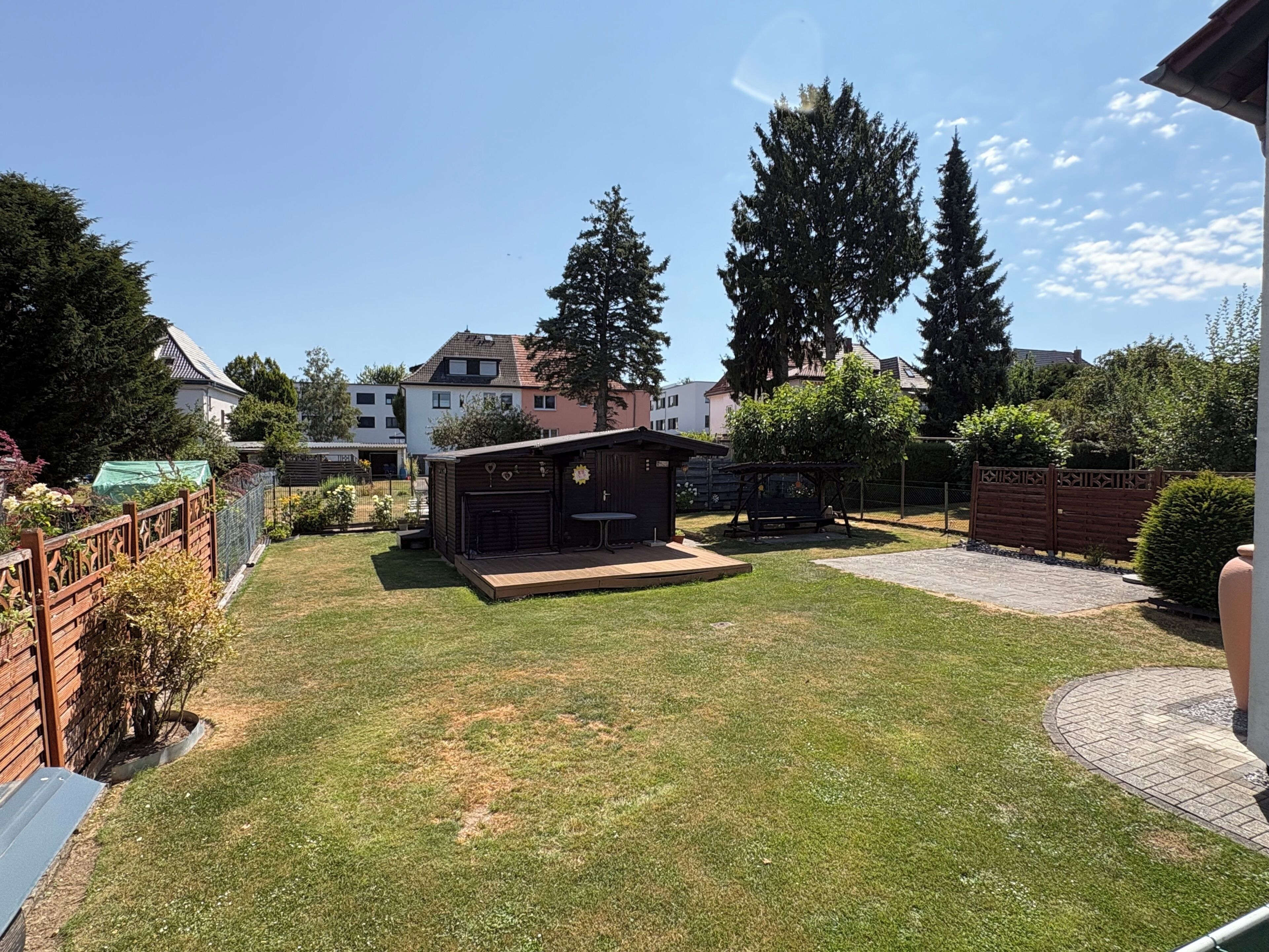 A backyard with a small wooden structure, a fenced area, and a paved walkway.