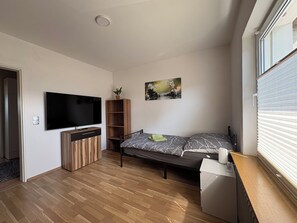 Un dormitorio moderno con televisión de pantalla plana, un armario de madera, una cama con ropa de cama estampada y un cuadro en la pared.