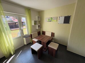 Una habitación con una mesa de comedor, sillas, un banco, una pizarra y una ventana con cortinas.