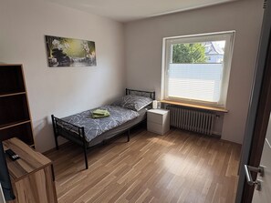 Ein kleines Schlafzimmer mit einem Einzelbett, einem Heizkörper, einem Fenster mit Jalousien, einem Bild an der Wand und einem Holzboden.