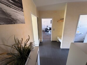 Ein Flur mit einem Blumentopf, einer Bank und Blick in einen Wohnbereich mit einer Couch und einem Teppich.