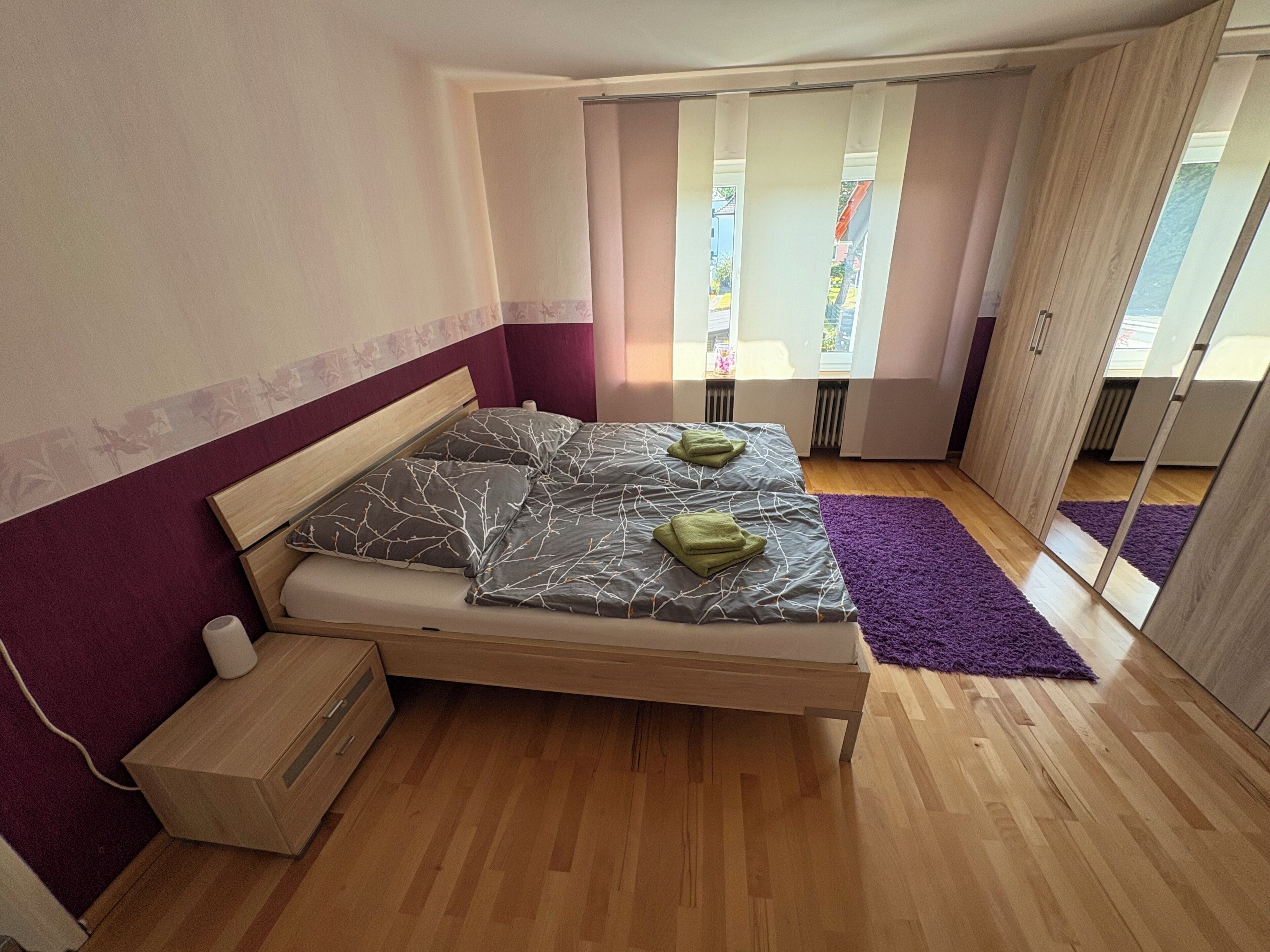 Ein Schlafzimmer mit einem Bett, einem Nachttisch aus Holz und einem violetten Teppich.