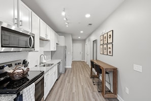 A modern kitchen with white cabinets, a stainless steel microwave, and a wooden dining table.