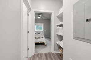 A narrow hallway leading to a bedroom with a bed, a ceiling fan, and a window.