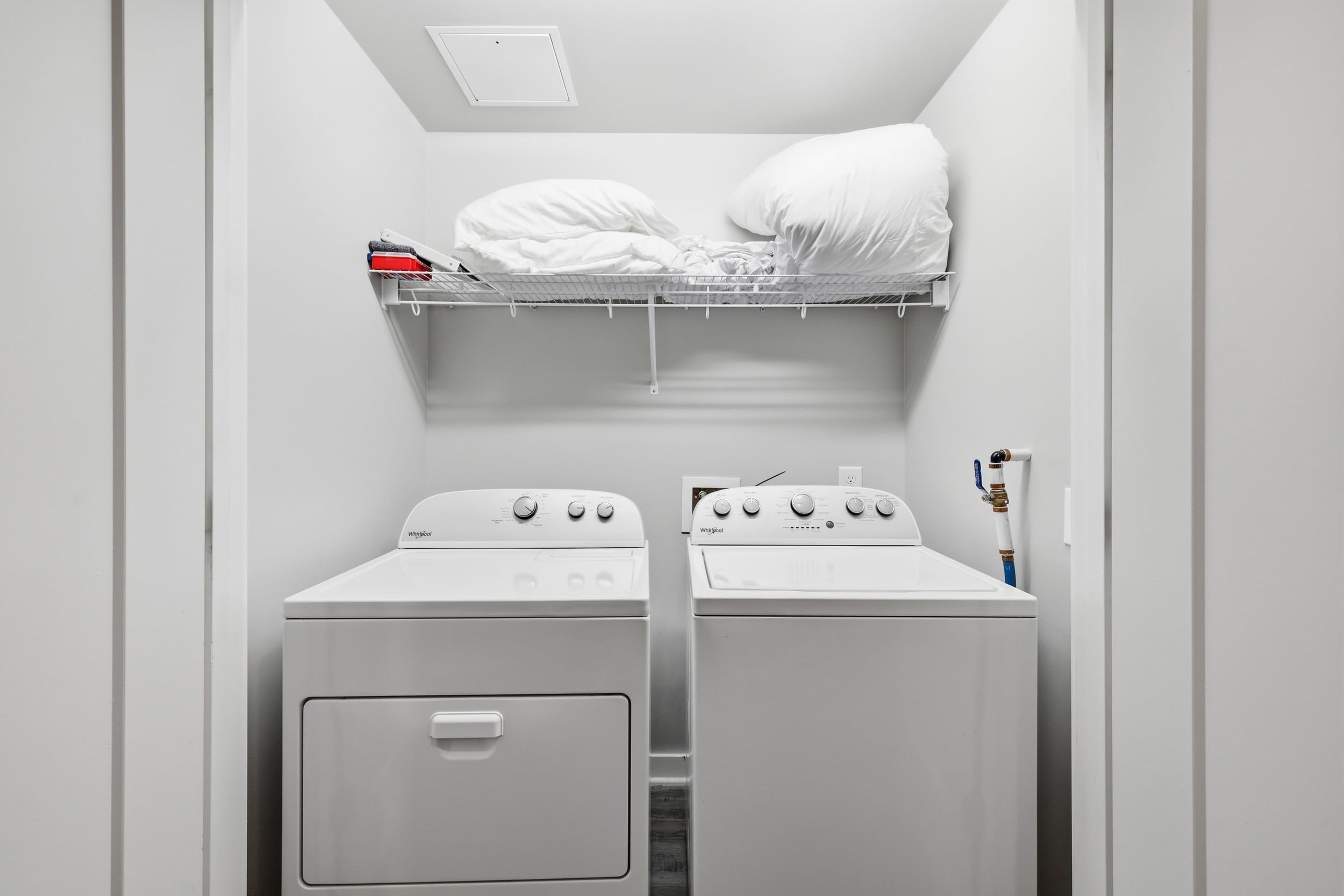 A compact laundry room with a washing machine and dryer, a small shelf above the dryer, and a white door.