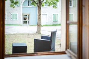 Vista desde una habitación con ventana que da a un edificio con múltiples ventanas y un árbol.
