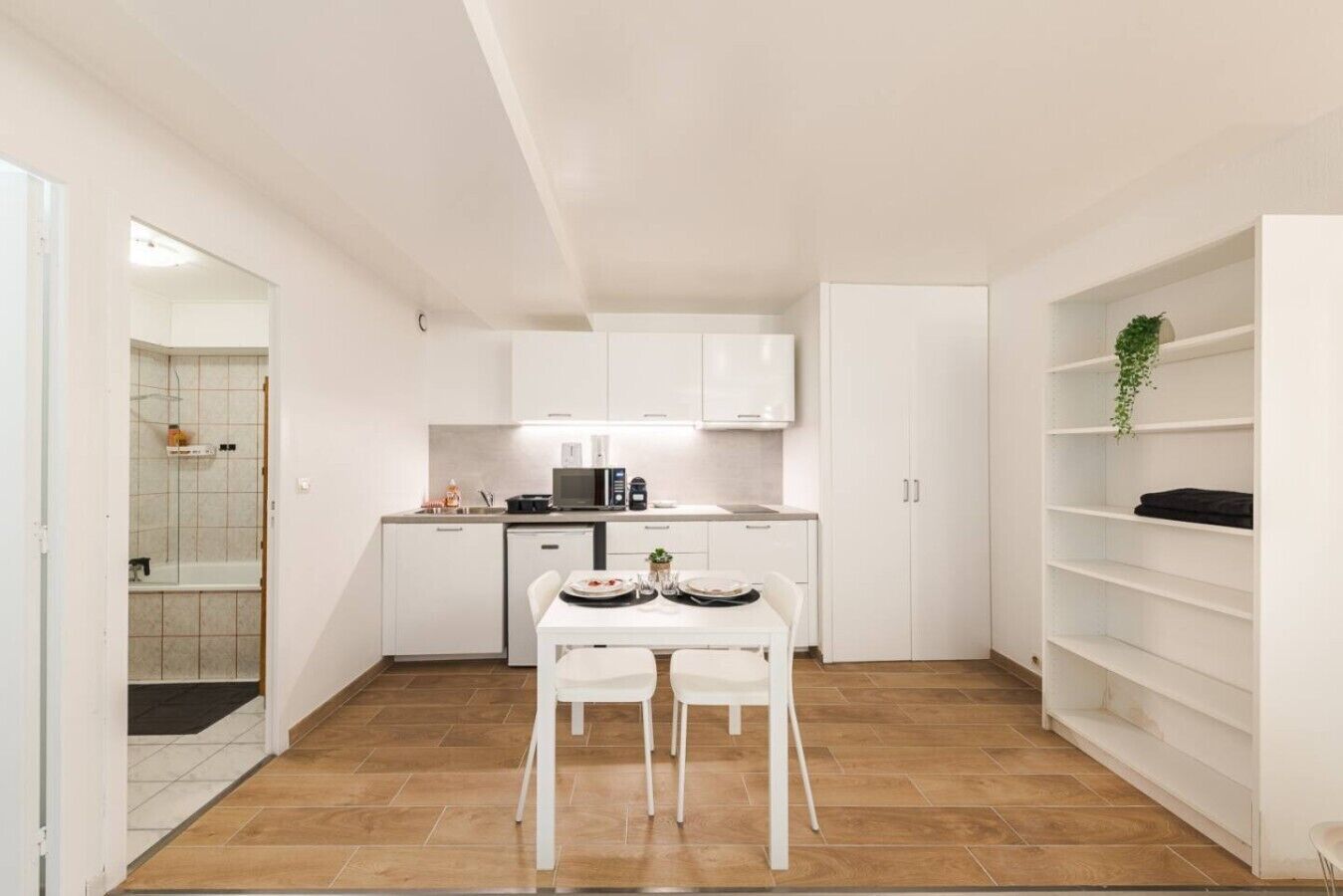Cocina compacta con muebles blancos, una mesa de comedor con sillas y una pequeña isla.
