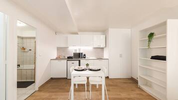 Cocina compacta con muebles blancos, una mesa de comedor con sillas y una pequeña isla.