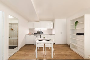 Cocina compacta con muebles blancos, una mesa de comedor con sillas y una pequeña isla.