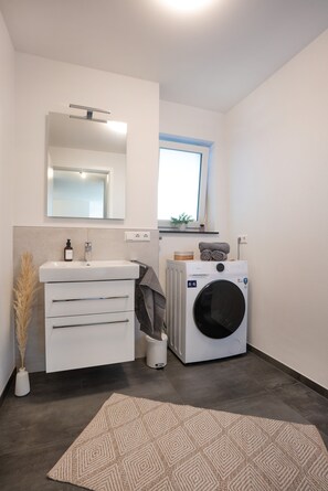 A modern bathroom with a white sink, mirror, and a built-in washing machine.