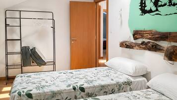 Un dormitorio con dos camas, un tragaluz, una puerta de madera, un mural en la pared y un perchero con ropa.