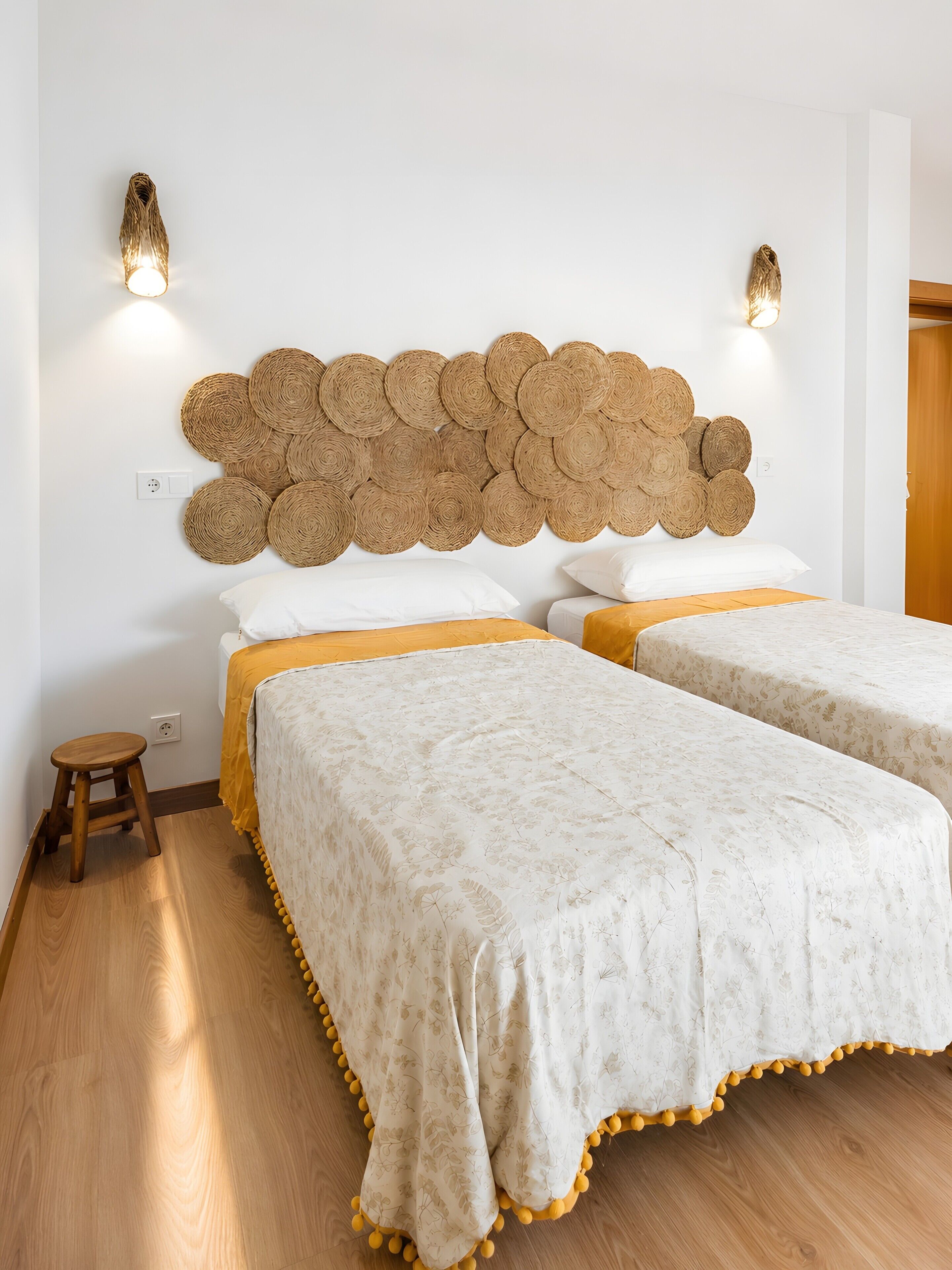 Un lit double avec une tête de lit en matière tissée, deux tables de chevet et un luminaire fixé au mur.