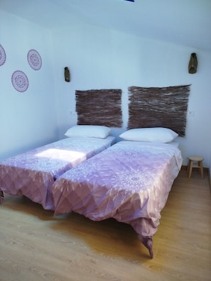 A room with two beds, a small stool, and decorative wall art.