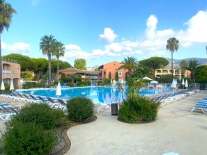 A pool area with lounge chairs and umbrellas, surrounded by greenery and buildings. - 2-Bedroom Apartment – On the Banks of the Siagne, with Pool & Parking (Mandelieu-la-Napoule)