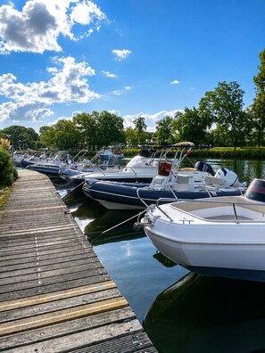 A wooden dock with several boats moored alongside a calm body of water, surrounded by trees. - 2-Bedroom Apartment – On the Banks of the Siagne, with Pool & Parking (Mandelieu-la-Napoule)