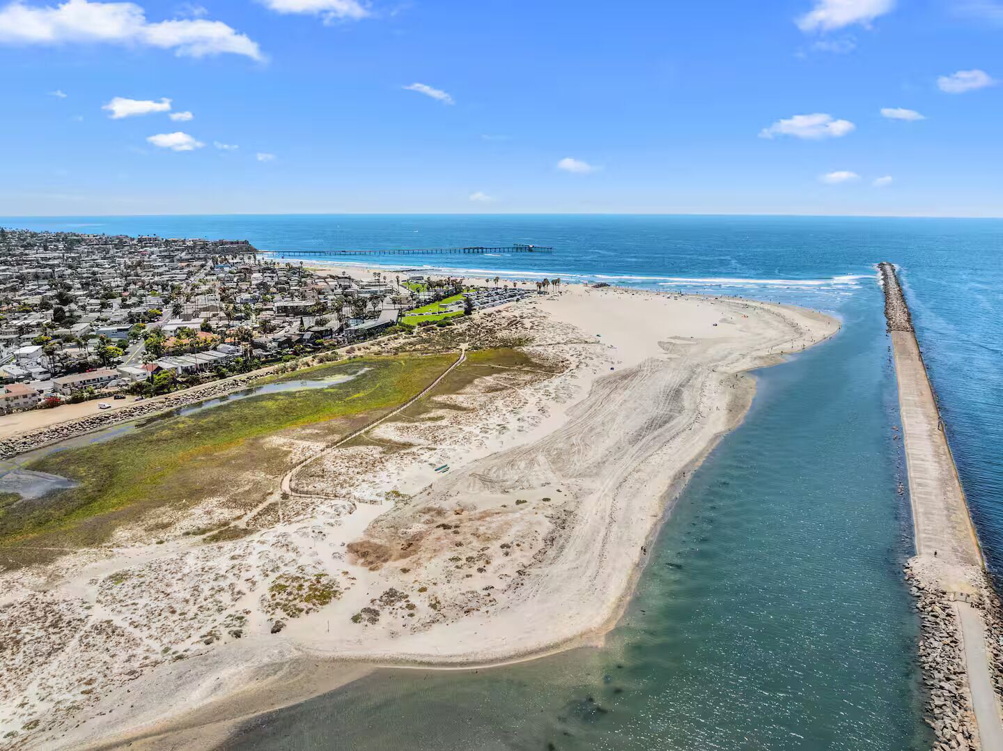 Vista aérea de una zona costera con playa, muelle y área residencial.