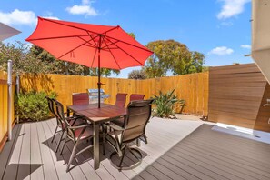 Una terrassa amb taula i cadires, un parasol vermell i una barbacoa.