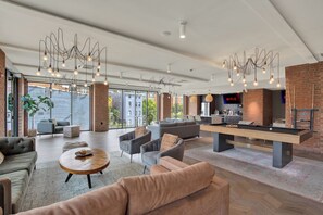 A modern lounge area with sofas, a pool table, and a bar area with a television screen. - Chic 1BR Suite | Downtown CIN | Pool & Gym (Cincinnati)