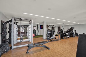 Ein moderner Fitnessraum mit verschiedenen Trainingsgeräten, darunter ein Squat-Rack, eine Bankpresse und Cardiogeräte.