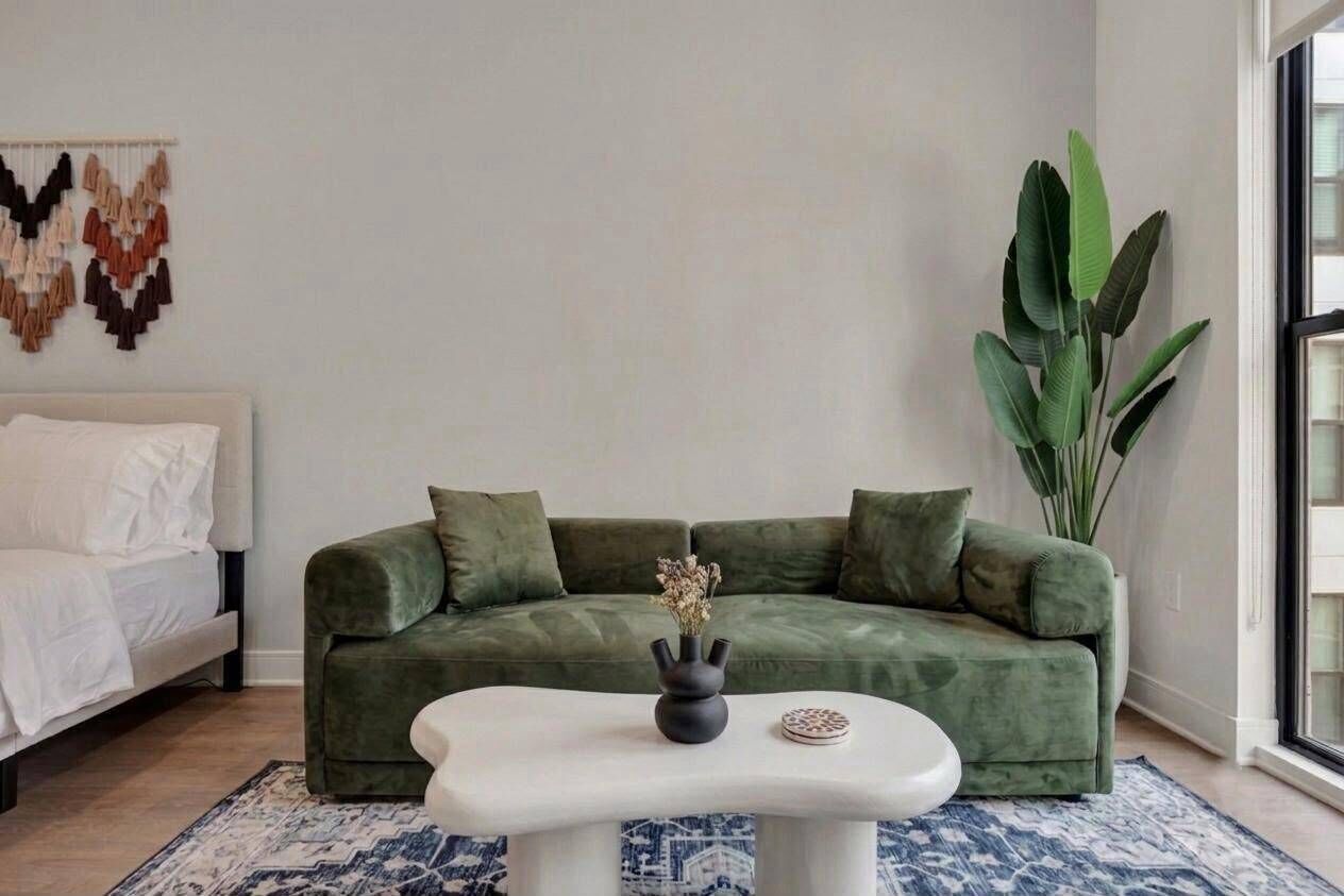 Een moderne woonkamer met een groene bank, een witte salontafel en een grote plant.