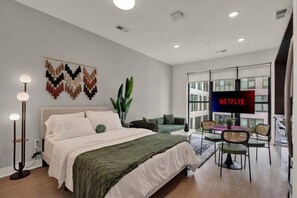 Ein modernes Schlafzimmer mit Bett, Nachttischlampe und an der Wand montiertem Fernseher, der 'NETFLIX' zeigt.