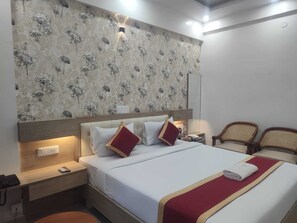 A hotel room with a bed, bedside tables, a nightstand, a lamp, and two chairs.