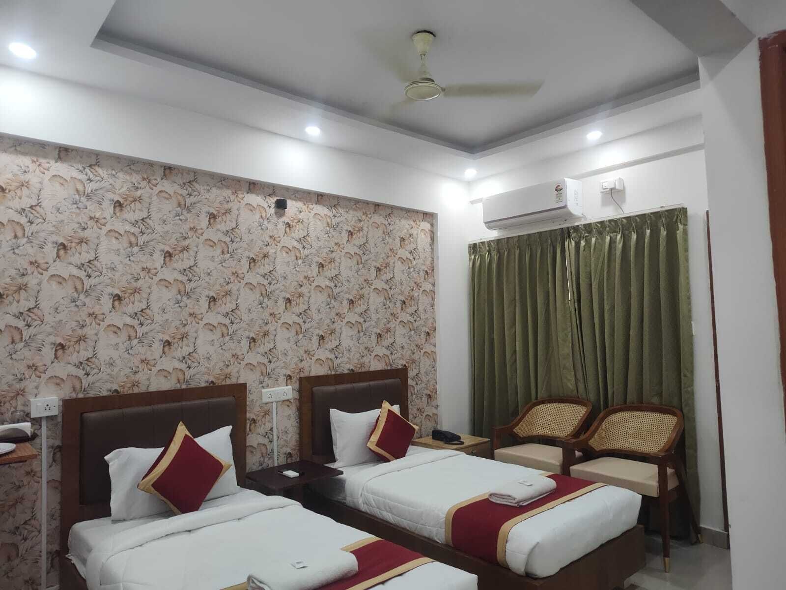 A hotel room with two beds, a ceiling fan, an air conditioning unit, a green curtain, and a seating area with chairs.