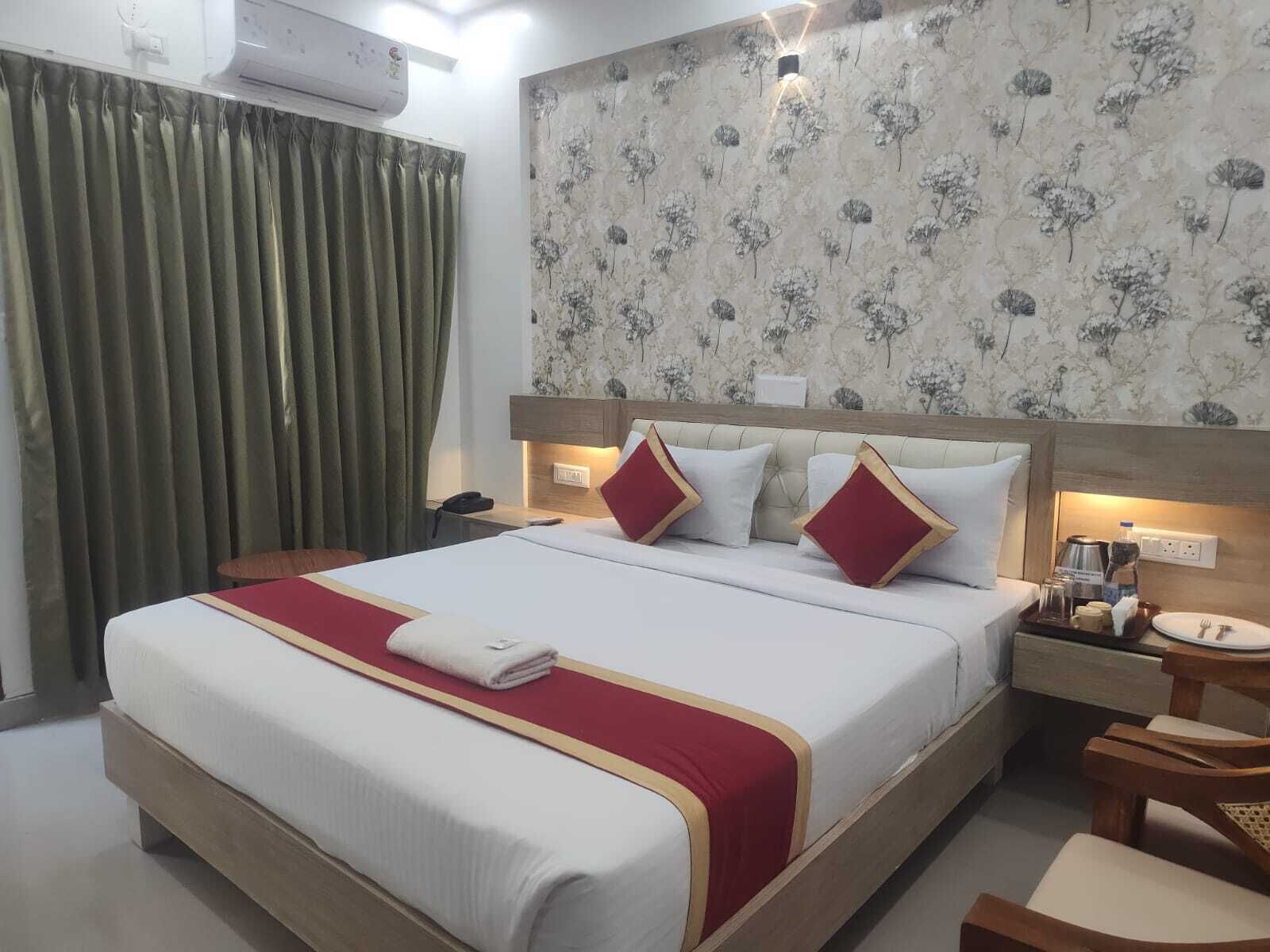 A hotel room with a large bed, a bedside table, a nightstand, a chair, and a wall-mounted air conditioner.