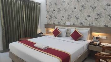 A hotel room with a large bed, a bedside table, a nightstand, a chair, and a wall-mounted air conditioner.